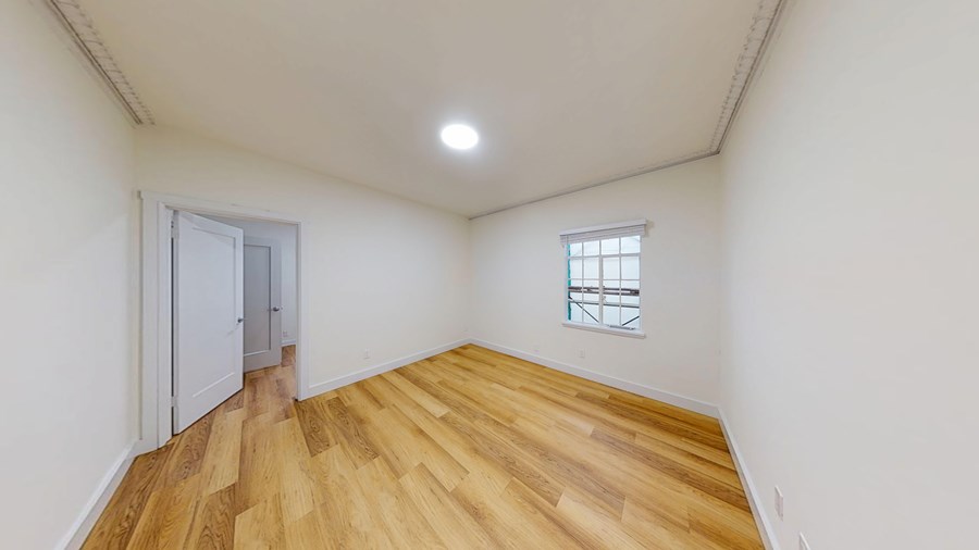 A room with wooden flooring and a window with bars on it.